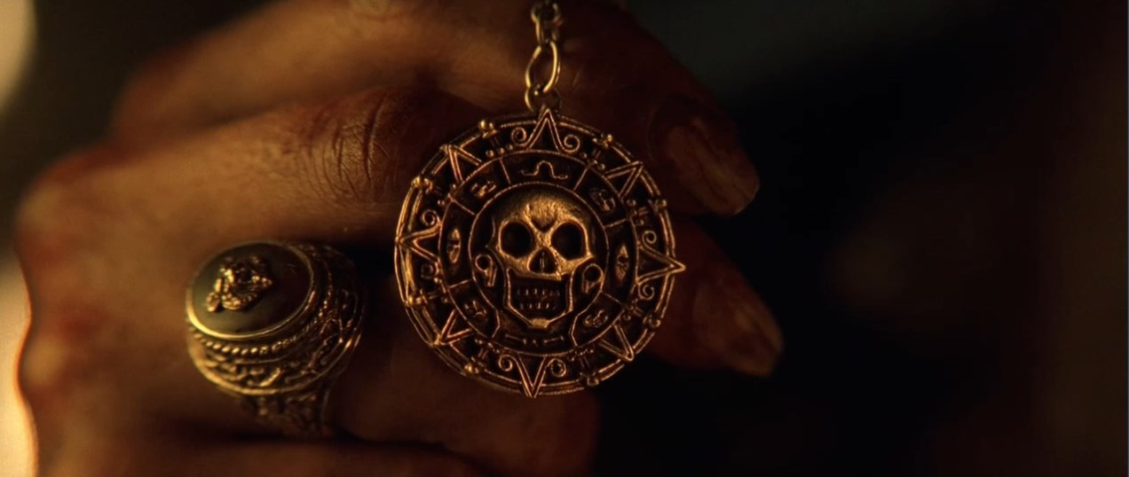 Элизабет Суонн Капитан Гектор Барбосса — Вы не знаете, что это такое? Верно?
— Пиратский медальон.
— Это ацтекское золото, одна из шестисот шестидесяти трёх бляшек, что индейцы отнесли Кортесу как выкуп... выкуп за кровь, доставленный с надеждой положить конец расправам. Но алчность Кортеса была неутолима, и тогда языческие боги придумали страшное проклятие. Любой из смертных, кто возьмёт хоть одну золотую бляшку, обречён на вечные муки.